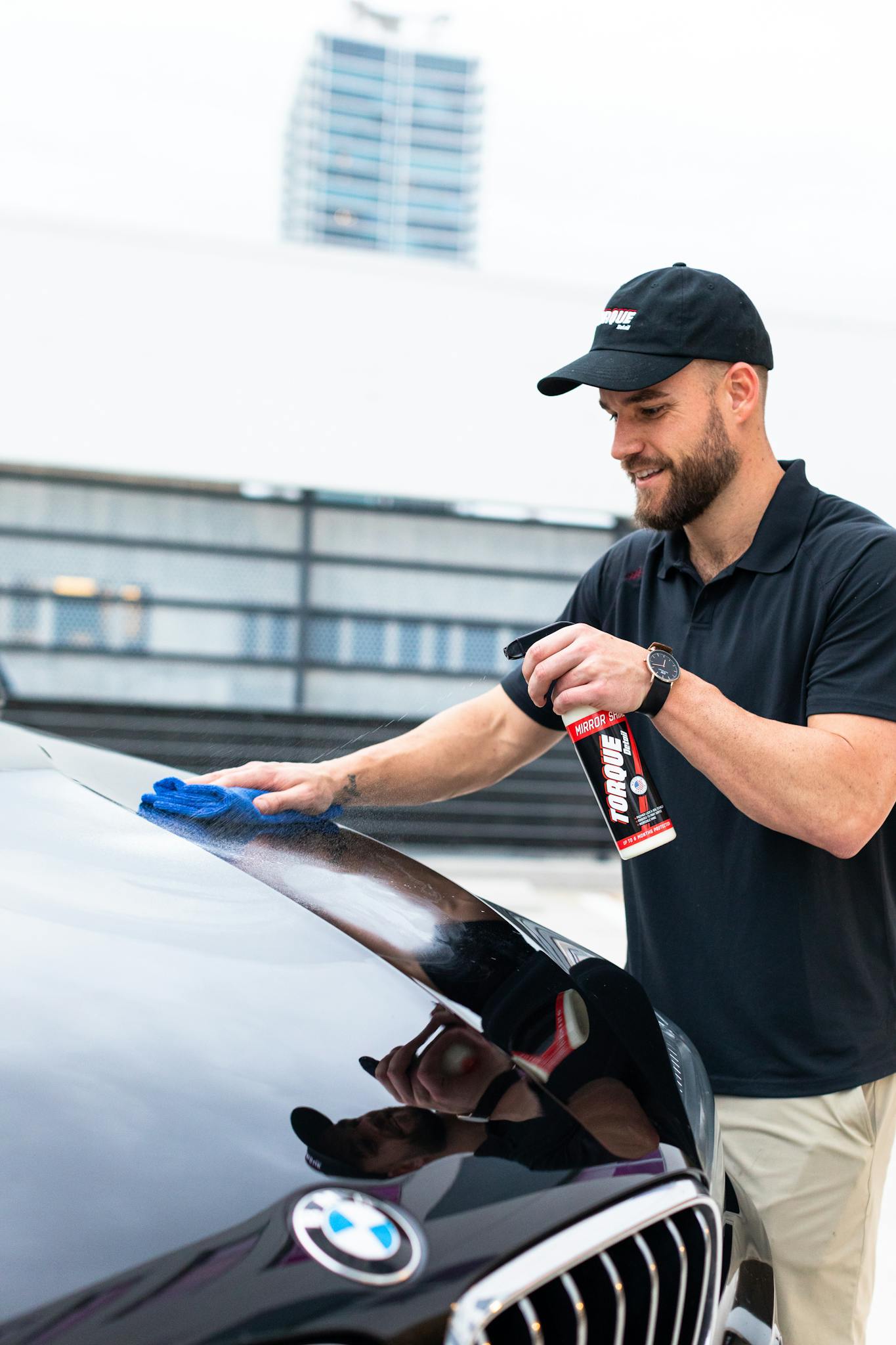 Man cleaning a BMW with a microfiber towel and spray outdoors. Perfect for automotive themes.